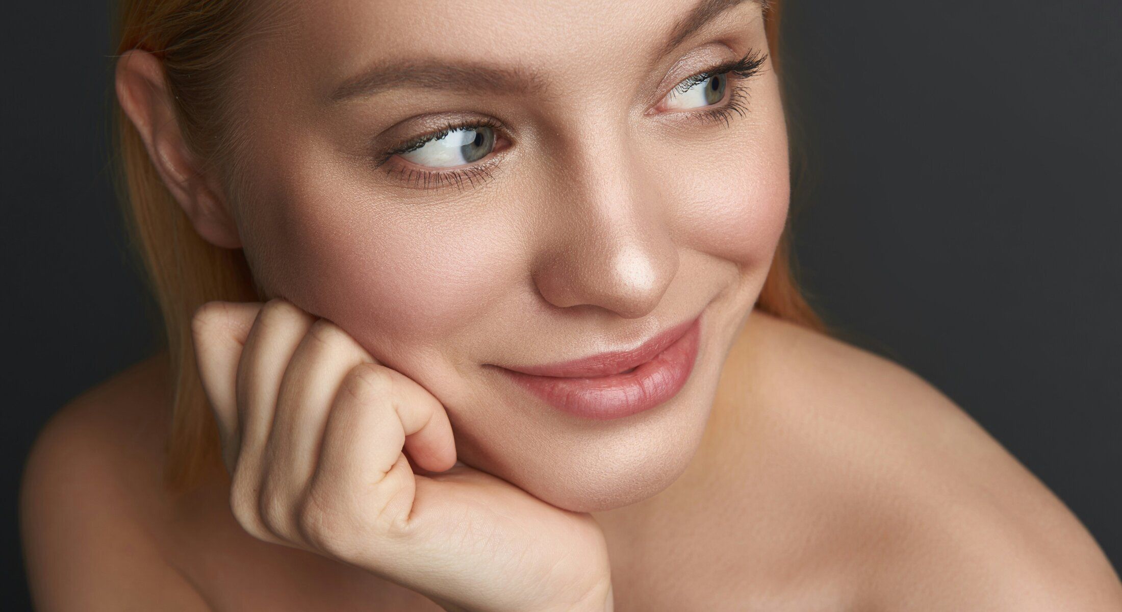 Close-up of a smiling woman with hand on chin.