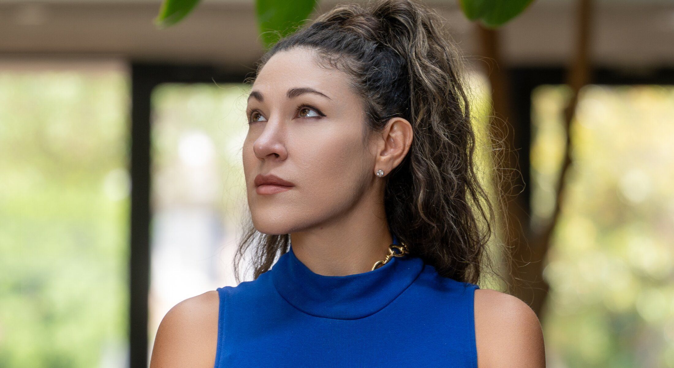 Woman in blue top looking thoughtfully upwards.