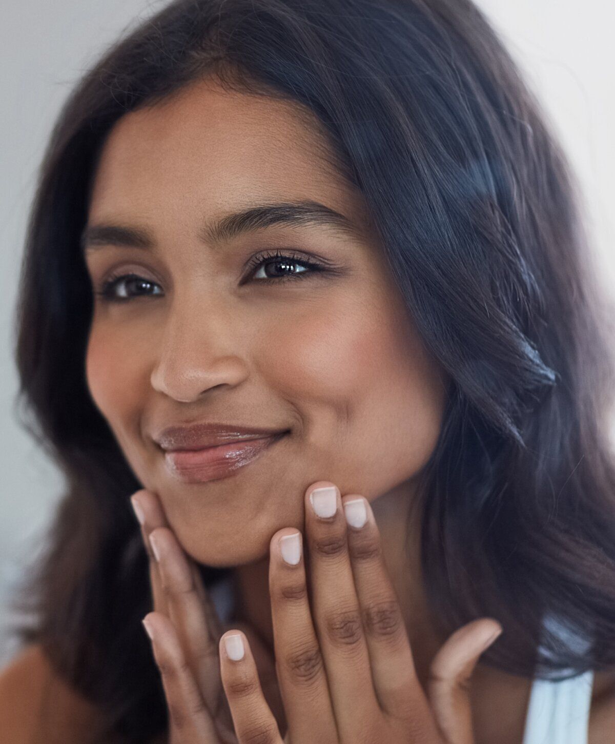 Smiling person with long, dark hair touching face.