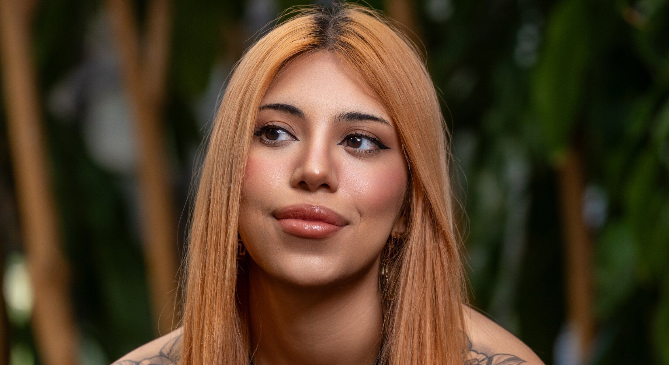 Person with long hair and tattoos smiling thoughtfully.