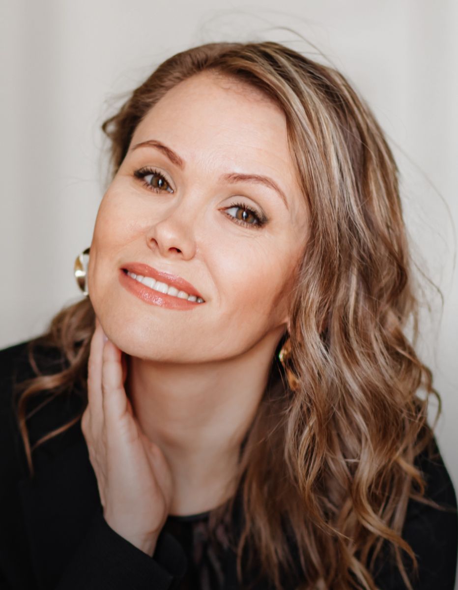 Smiling woman touching her neck, wearing earrings.