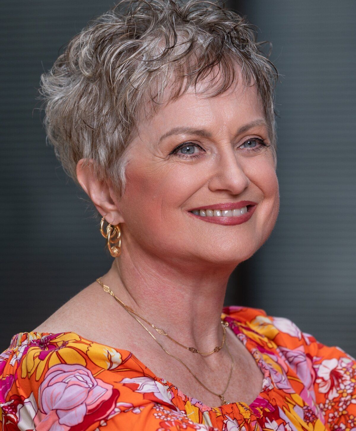 Smiling woman with short, stylish hair and colorful blouse.