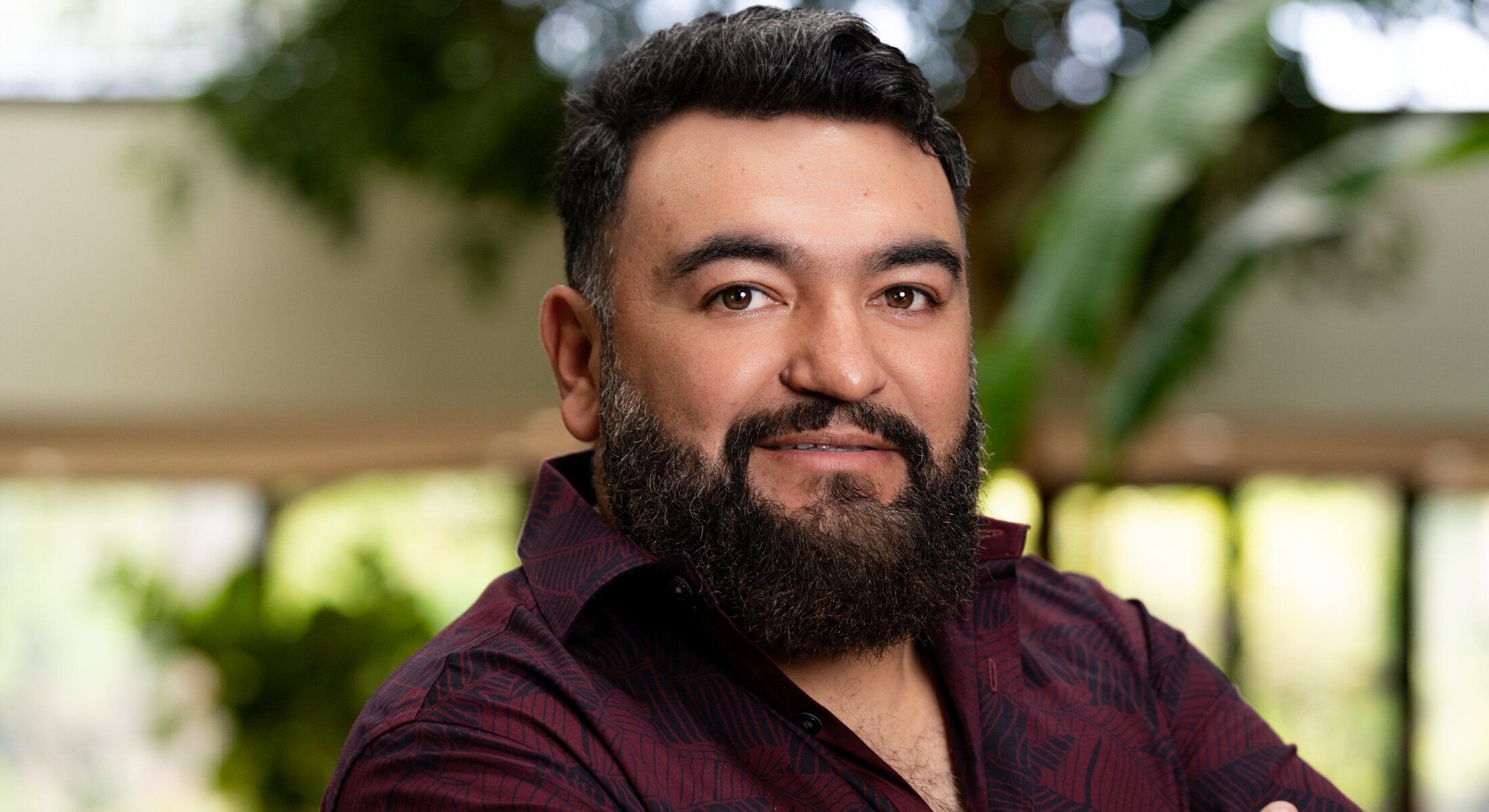 Man with beard smiling in a green environment.