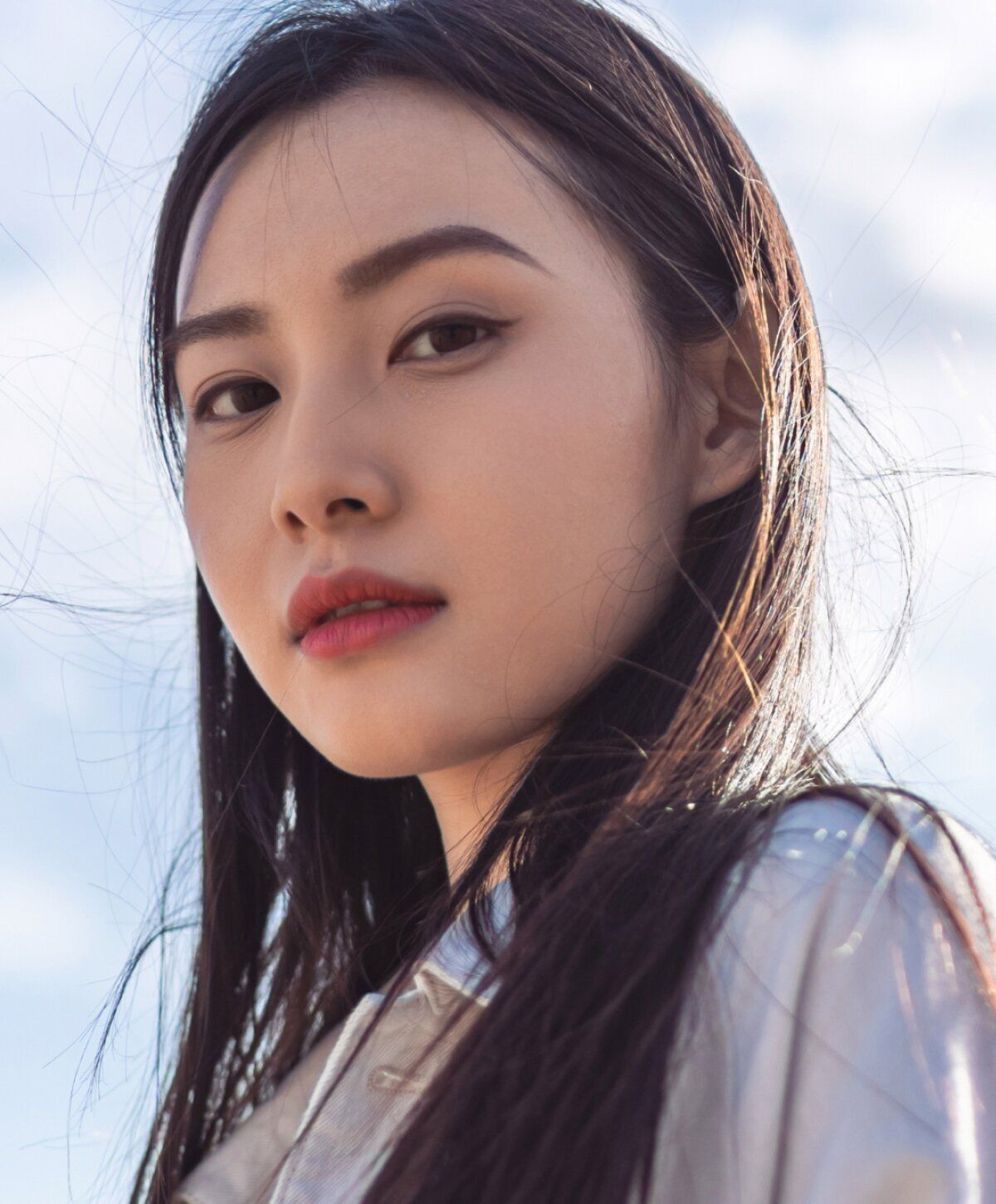 Woman with long hair against a cloudy sky.