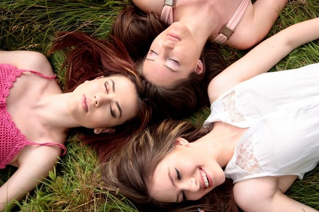 three women laying on the grass with their heads touching