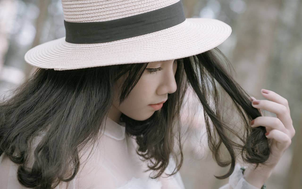 woman in hat looking to the side and touching her hair
