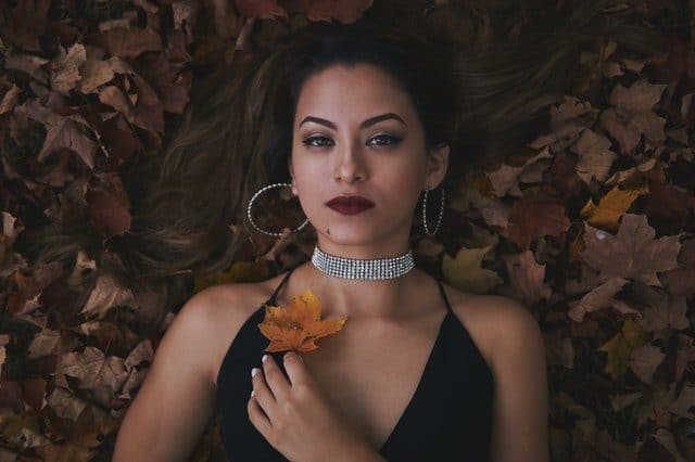portrait of woman laying in leaves with long brown hair and red lips
