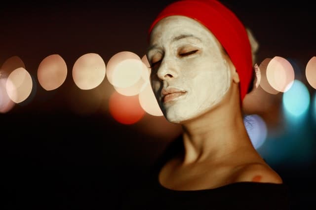 person with a clay face mask on their face, closing their eyes