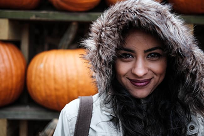 woman with olive skin smiling at camera with pumpkins in the background