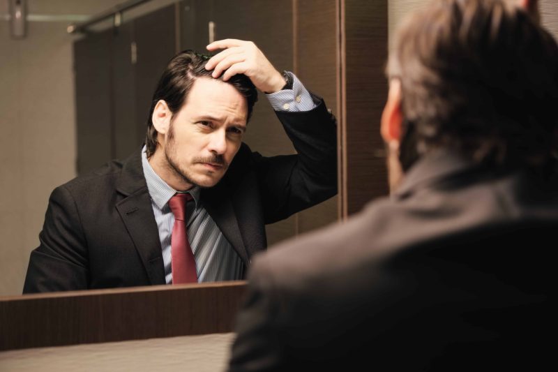 Business man in office bathroom. Stressed manager using restrooms, washroom and lavatories while looking at receding hairline. Male beauty in public toilet with businessman checking hair loss