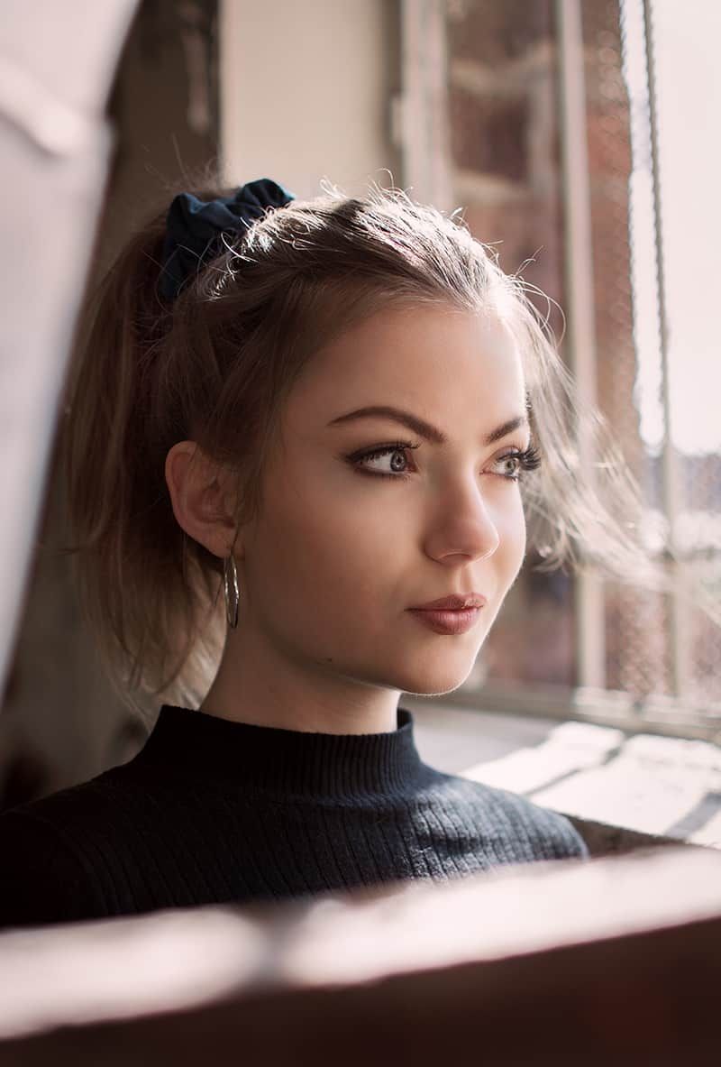 Portrait of a blonde-haired young woman wearing a black mock turtle neck sitting in a coffee shop.