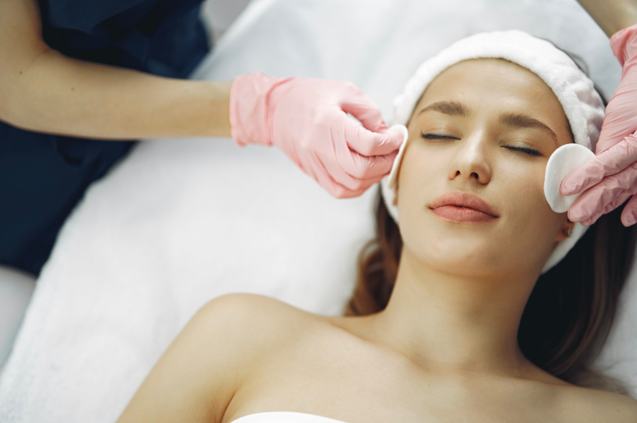 woman laying down with eyes closed and person with gloves wiping her face