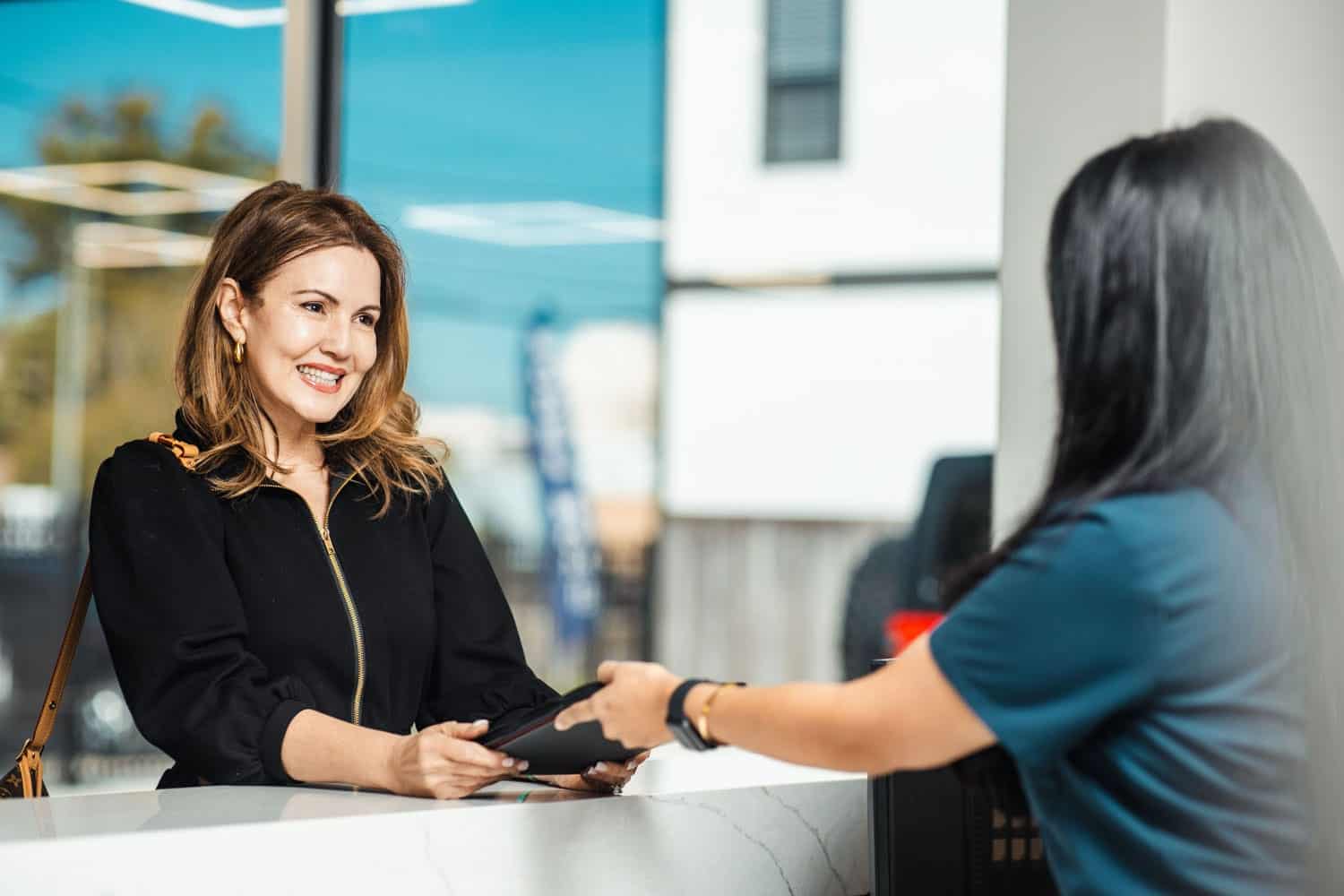 A facial plastic surgery patient smiling at a staff member at the Athré Facial Plastics front desk.