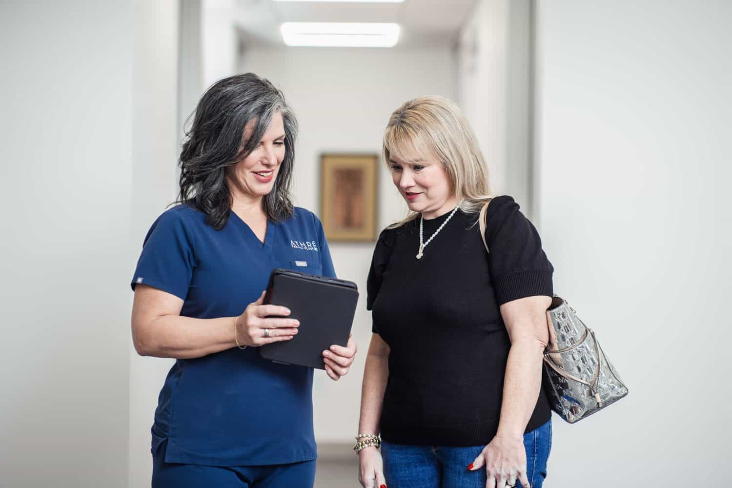 An Athré Facial Plastics staff member talking to a patient while viewing an iPad.