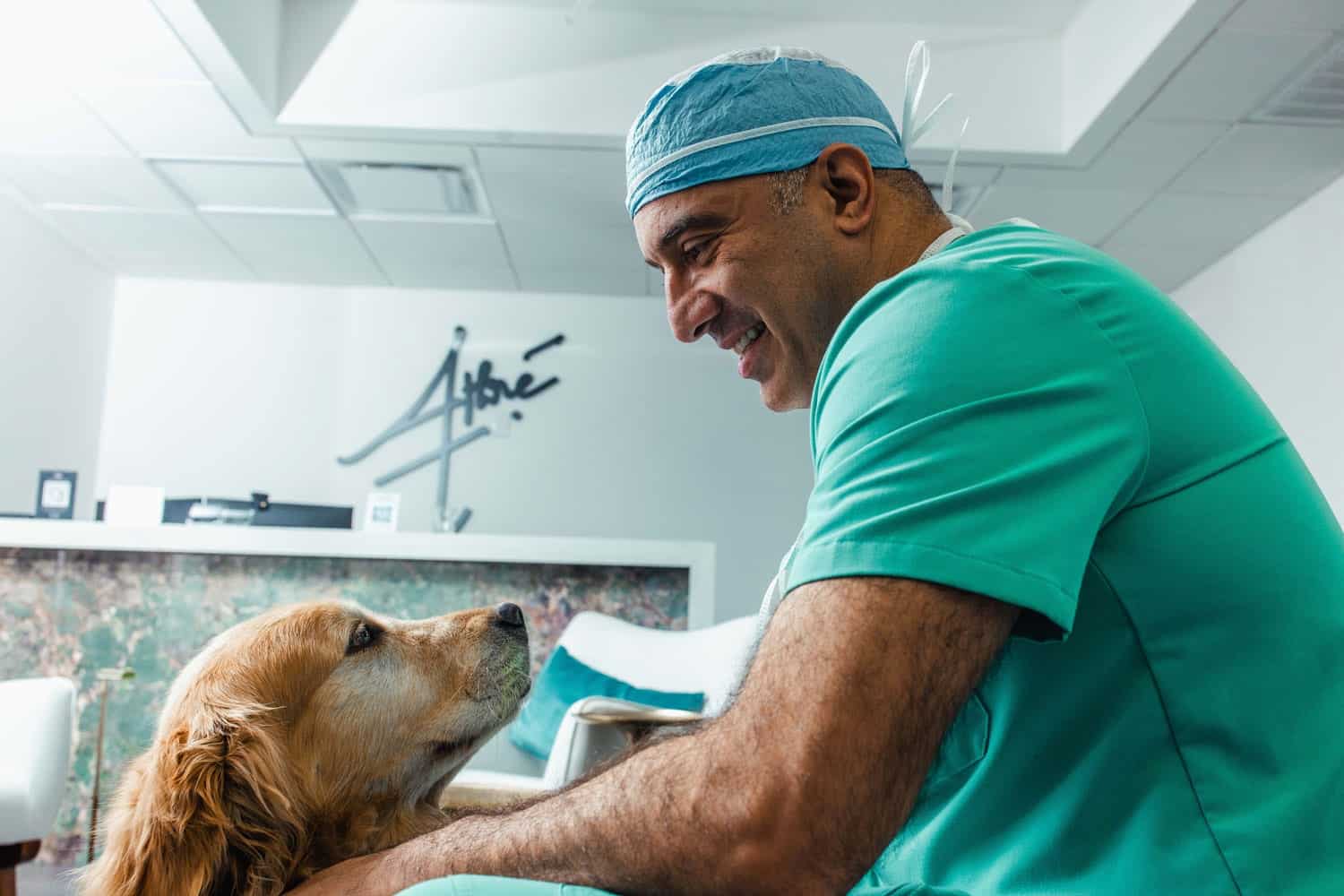 A man wearing surgical scrubs pets a golden retriever dog in a plastic surgeon lobby.