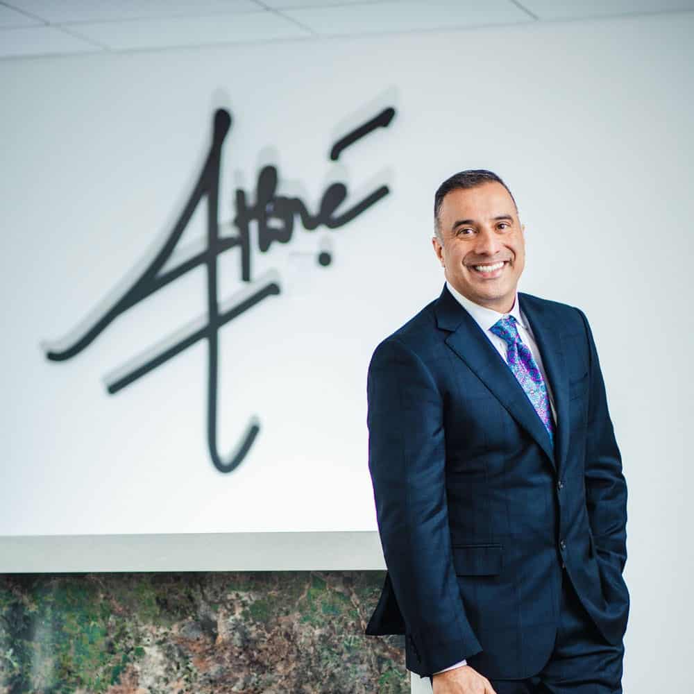 A man in a suit stands smiling next to a counter, with a stylized Athré logo on the wall behind him.