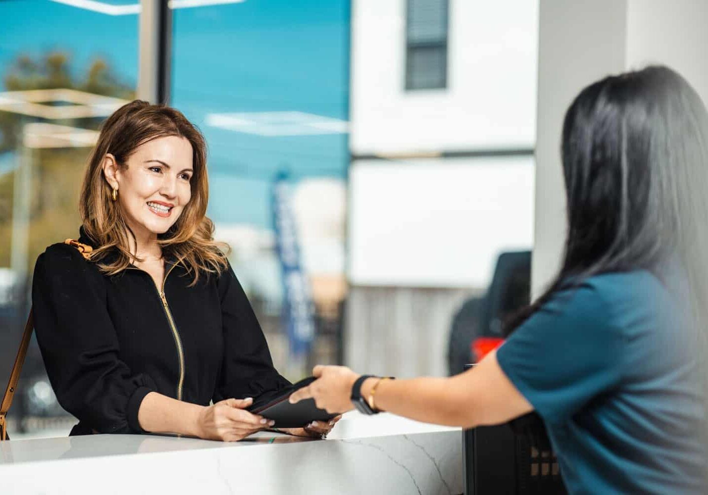 A facial plastic surgery patient smiling at a staff member at the Athré Facial Plastics front desk.