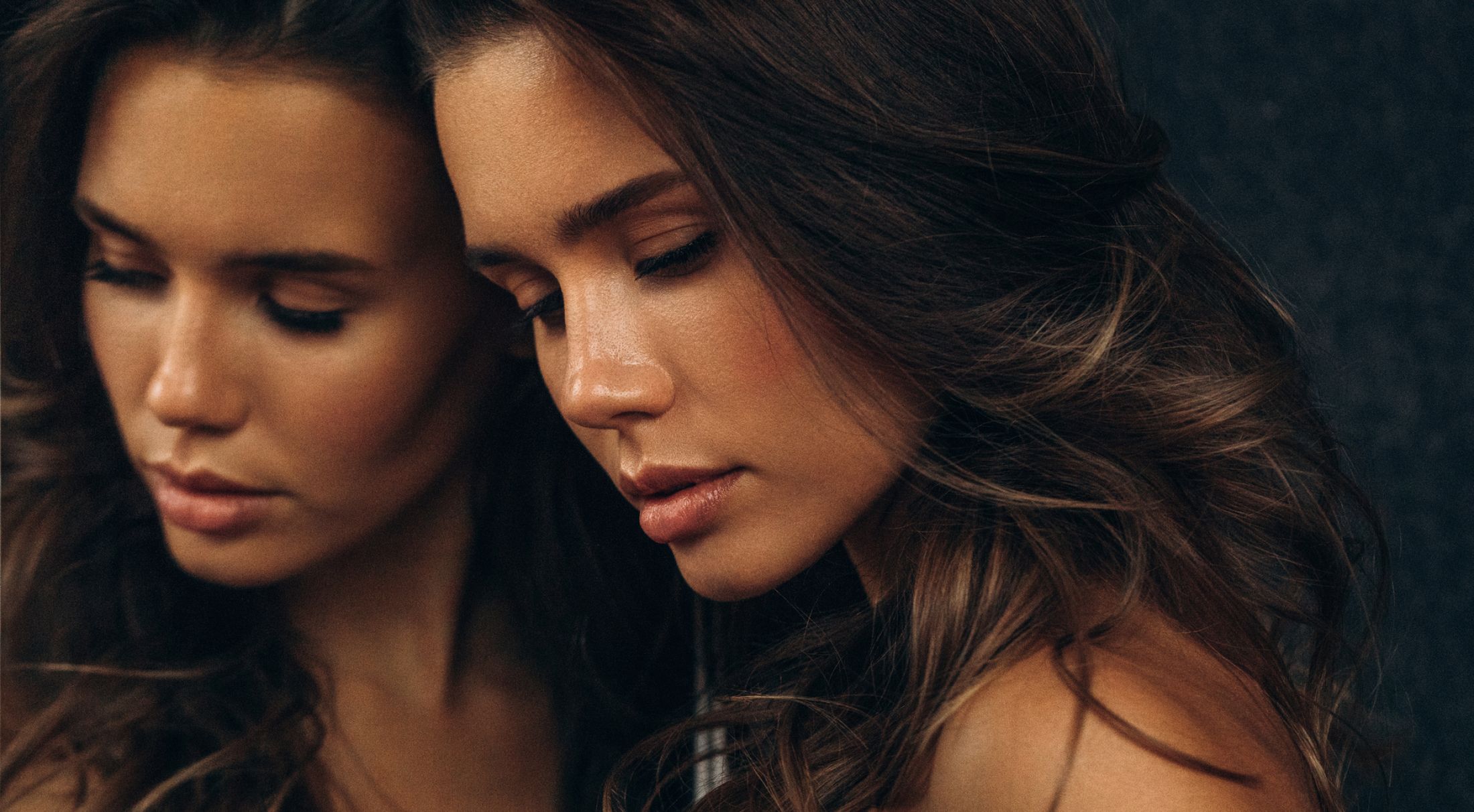 Woman with dark hair gazing thoughtfully at reflection.